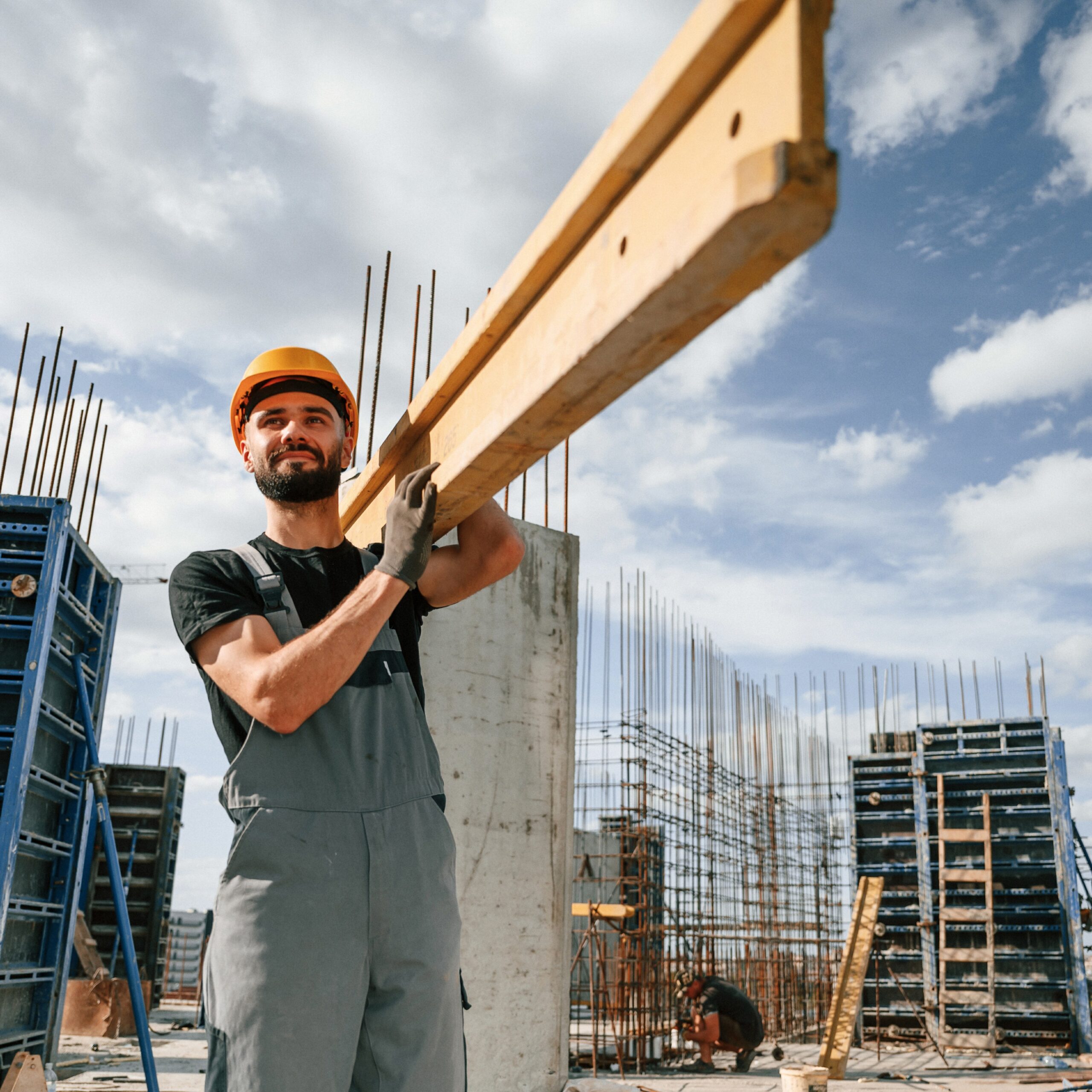 Front view. Carrying wooden plank. Man in uniform is working on the construction site.