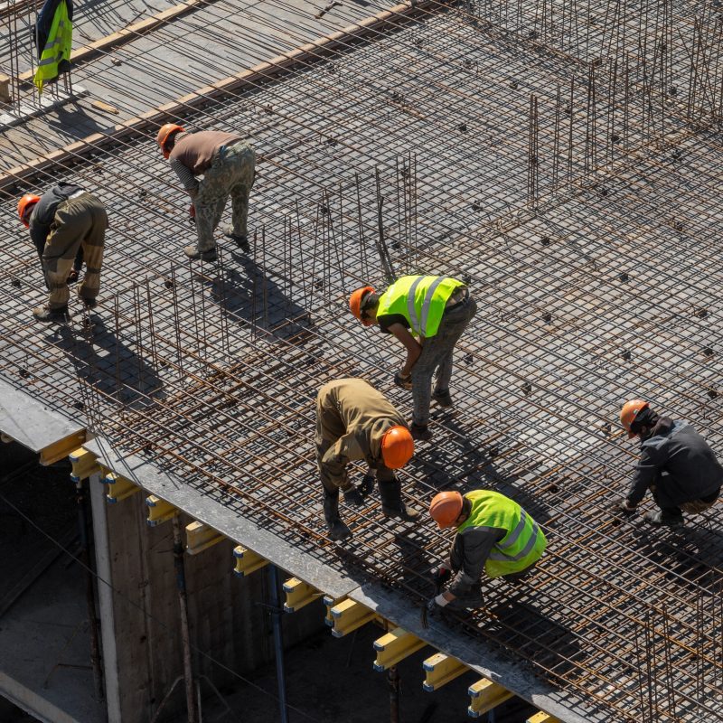 builders in hard hats and protective vests work at the construction site of a multi-storey building